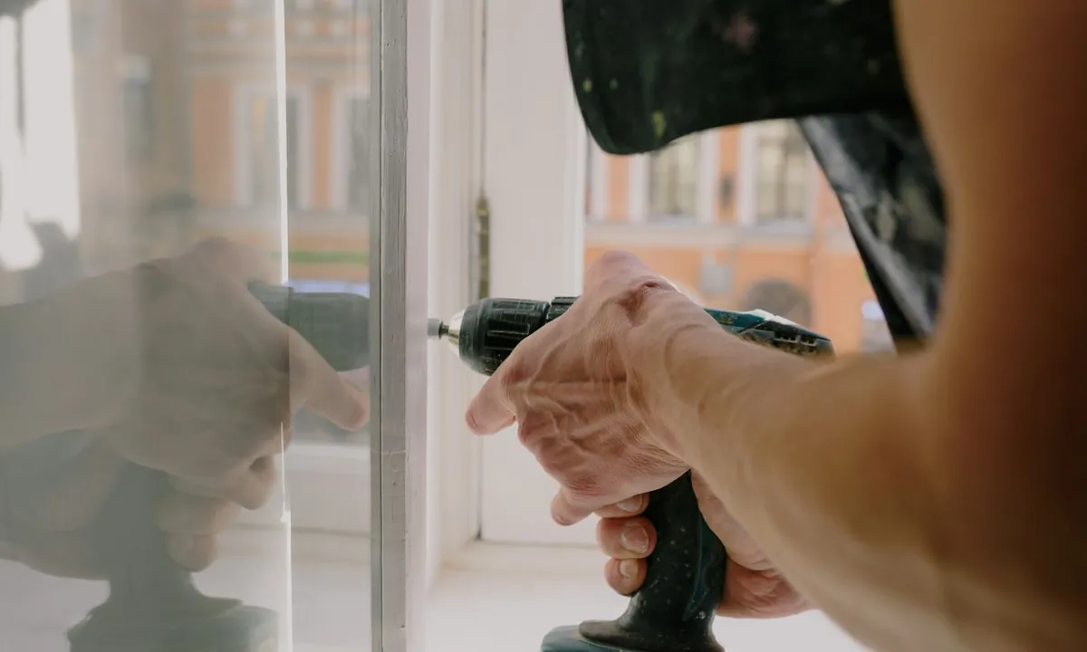 Réglage d’une fenêtre avec une visseuse, détail des mains et de l’outil